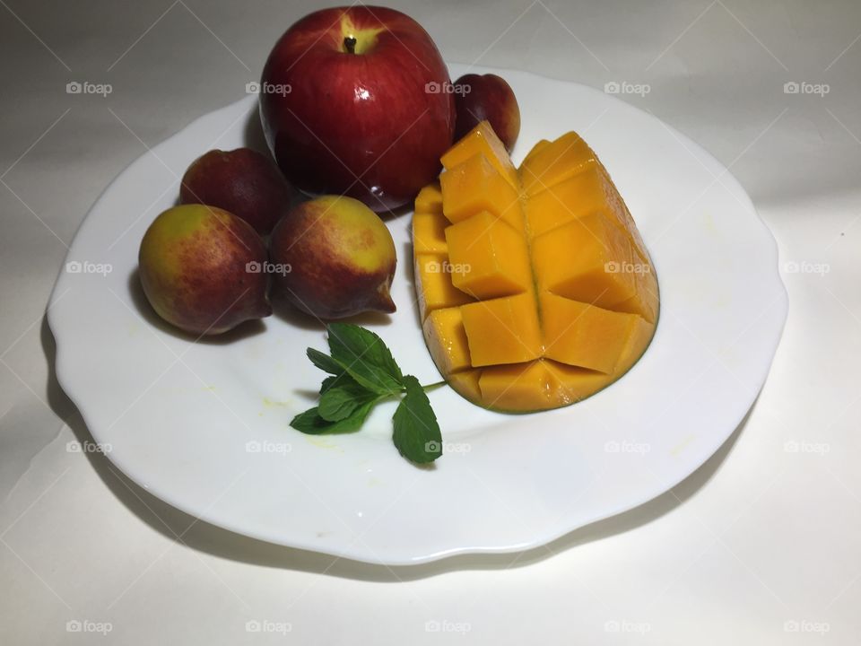 Red apple with mango fruit and peaches on white dish