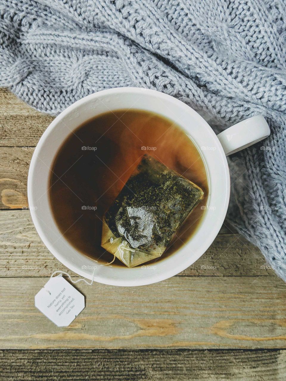 Flatlay style photo of a cup with tea and a sweater on a wooden background