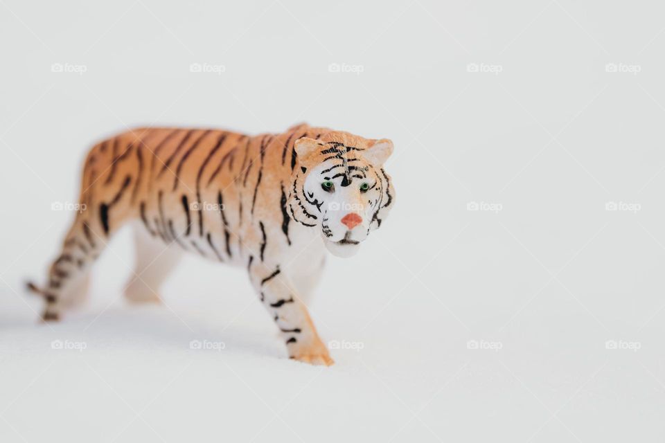 Portrait of one cute toy striped tiger walking in the snow, close-up side view.