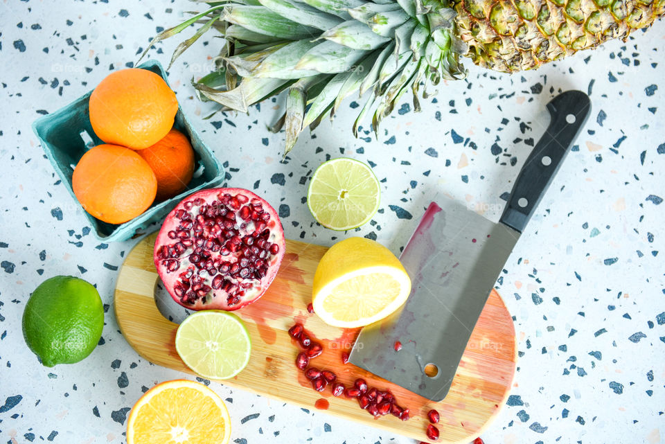 Flat lay of an assortment of colorful fruit on a kitchen countertop with a cutting board and a cleaver