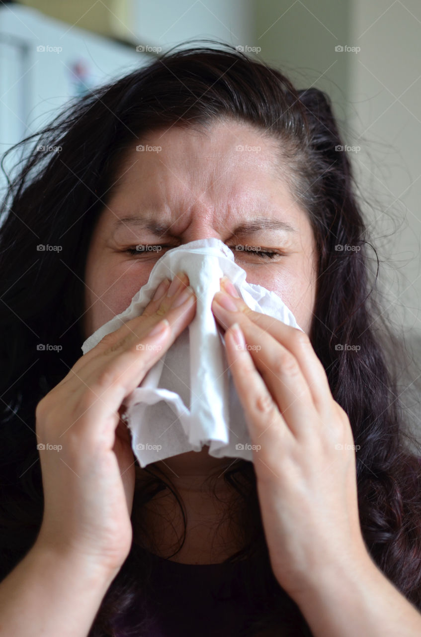 Woman blowing her nose hard into a tissue at home