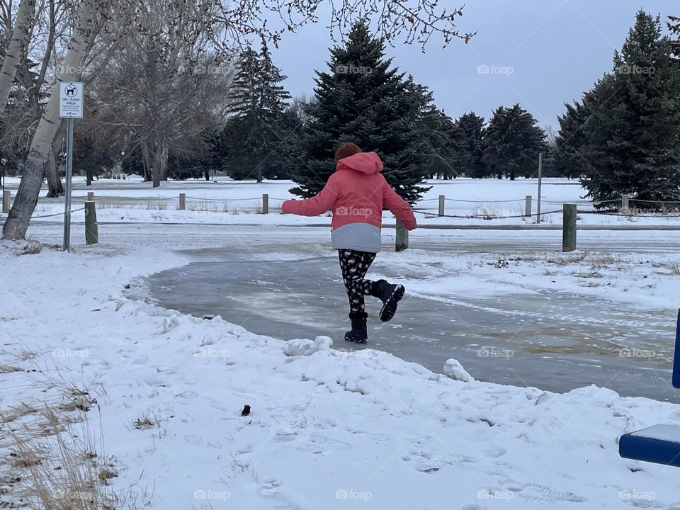 A young girl, making the best of a slippery, grey, winter day, in Alberta, Canada, by skating, sliding on some icy walk ways