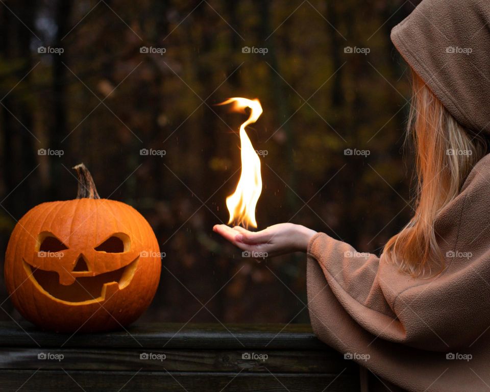 Flame pointing to a carved pumpkin, from a woman’s hand, to light the fall season