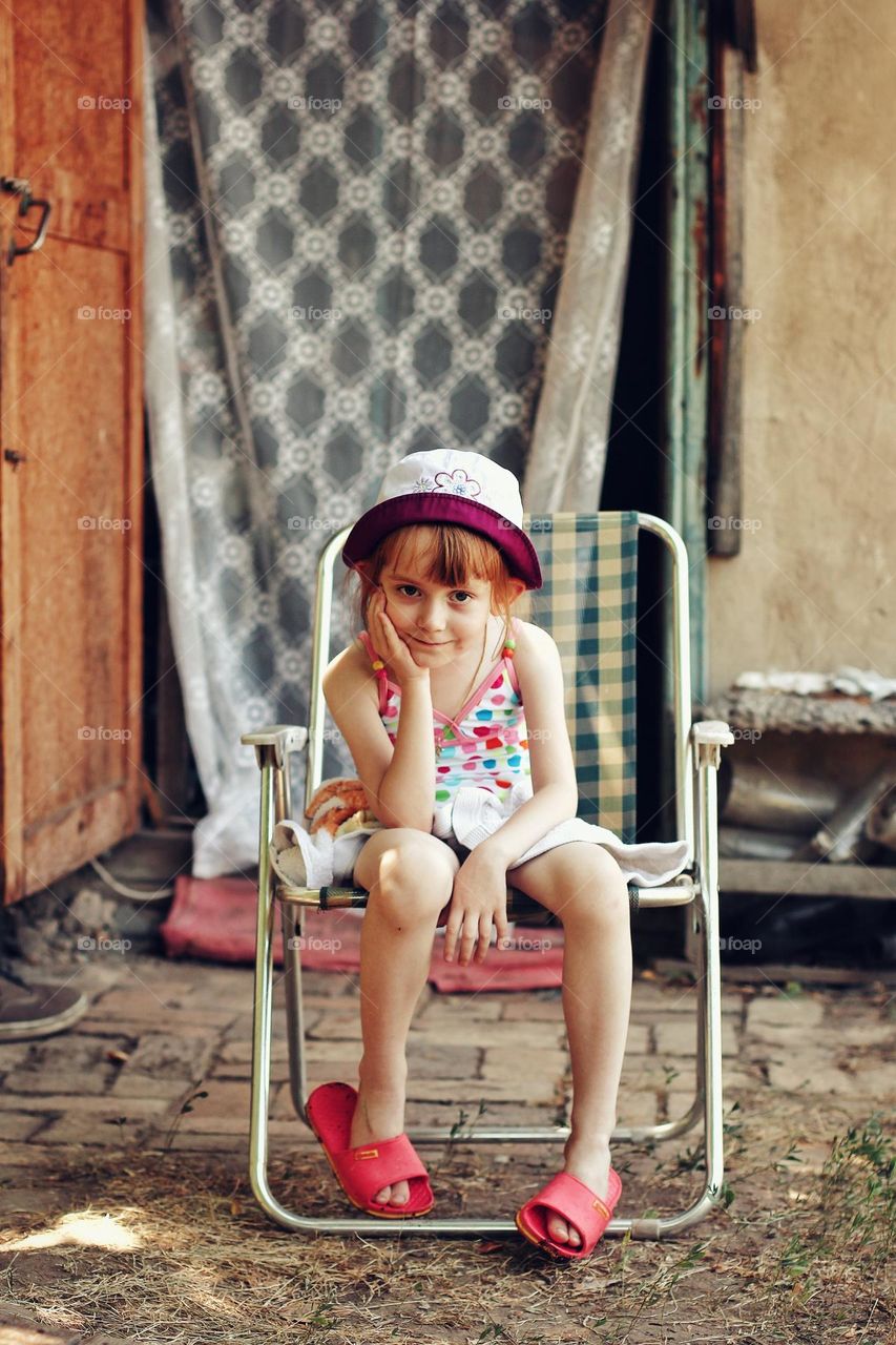 A girl is sitting on a sun lounger in a Panama hat and a swimsuit