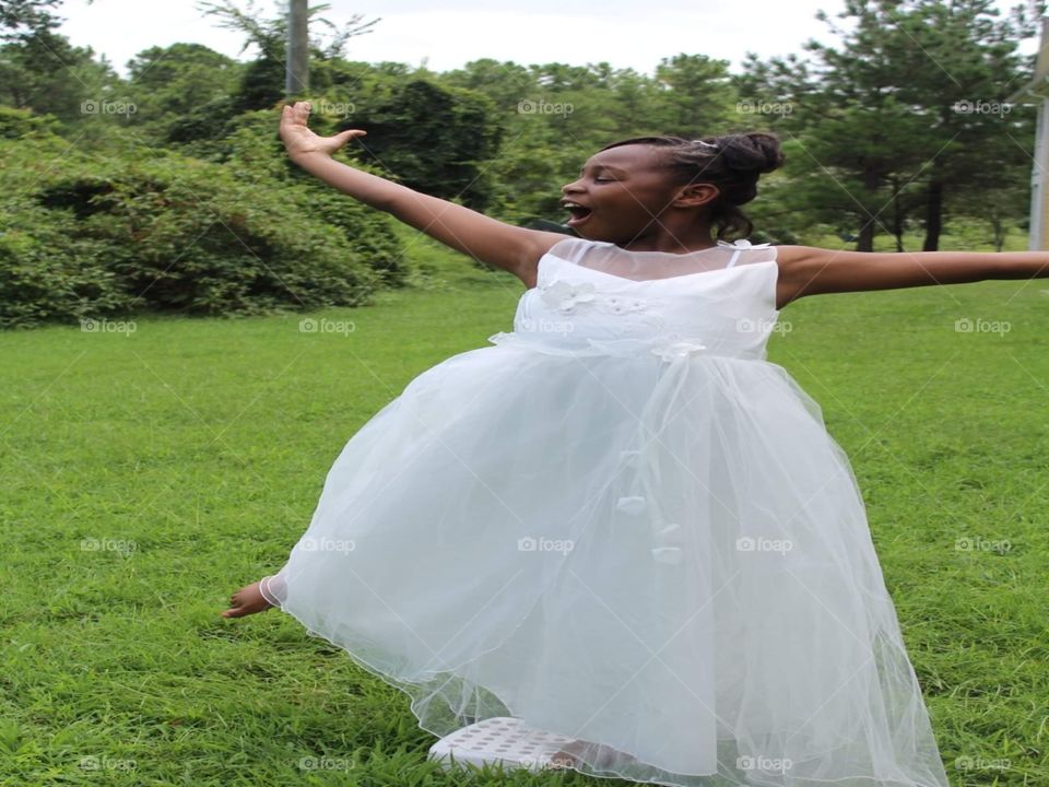 Young girl posing in a dance move with a white sleeveless dress outdoors