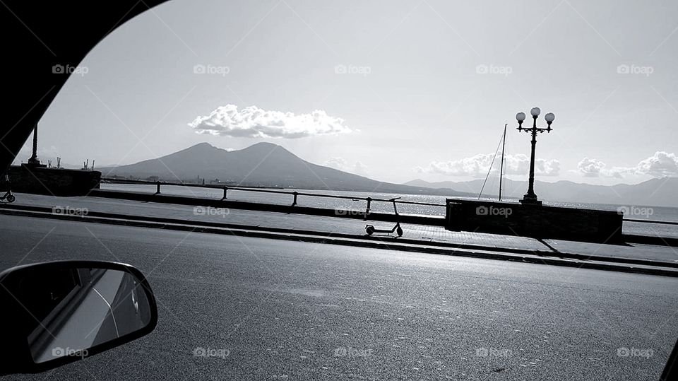 View from the side window of the car.  Sidewalk with a scooter.  Sea.  The mountains.  There is a cloud over the mountains.