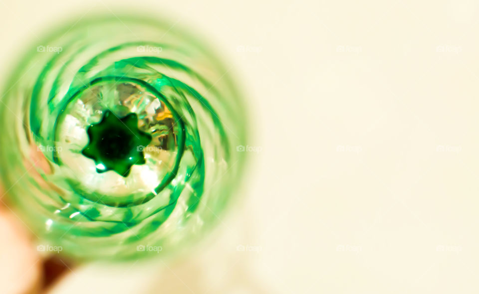 High angle view of green crystal champagne glass selective focus with green spiral reflection in glass on white isolated background 