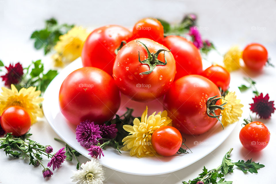 Fresh red tomatoes on a white plate decorated with colorful flower