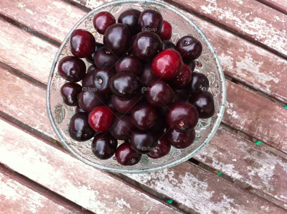 Glass bowl with red cherries standing on old worn wooden table outdoors in summer.