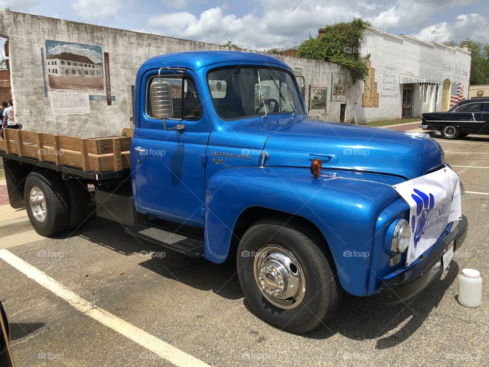 A vintage electric blue truck parked by old building. 