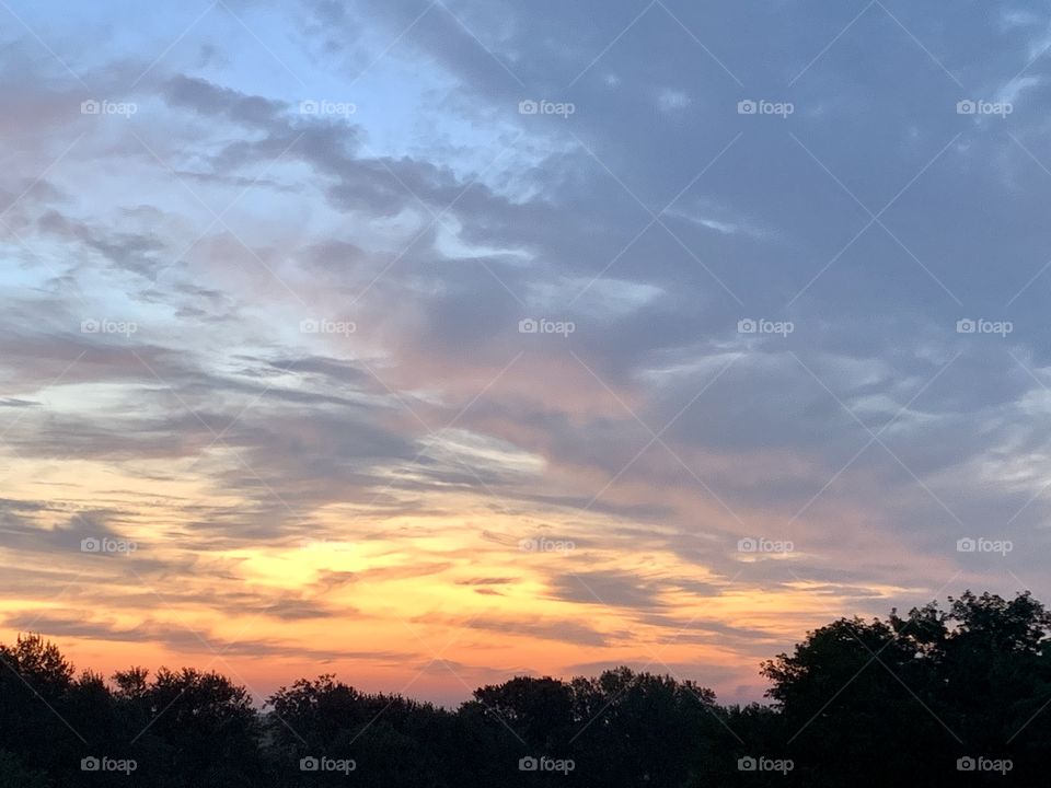 A colorful sky over a silhouetted line of trees