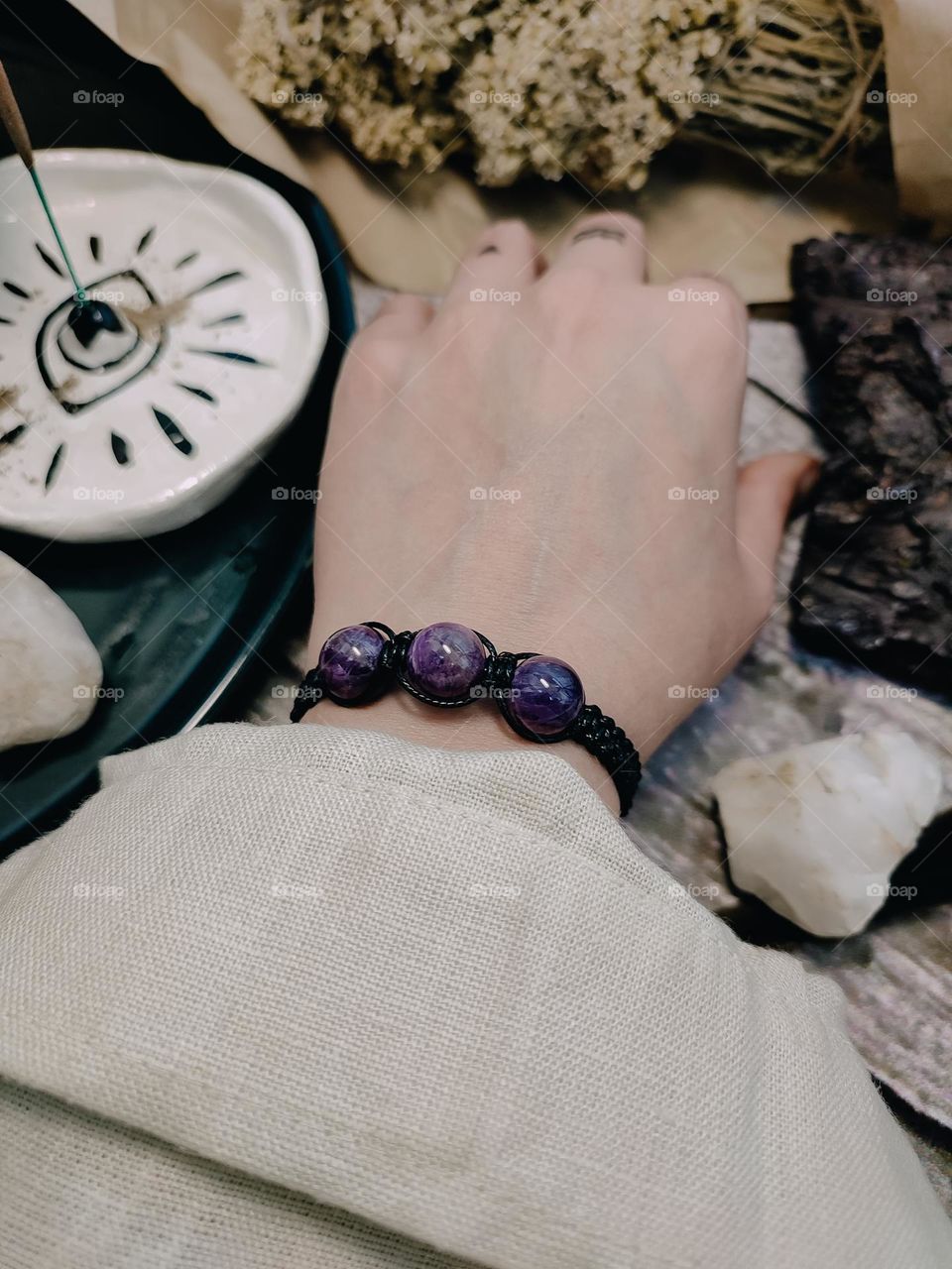 Meditation with herbs, minerals and aromatic sticks. Woman's hand in amethyst stone bracelet, magical symbols on fingers