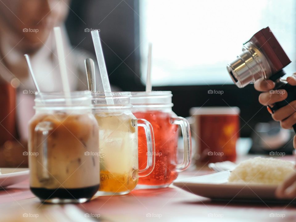 Close-up shot of a camera pointing to 3 mugs of fresh fruit juice on the table
