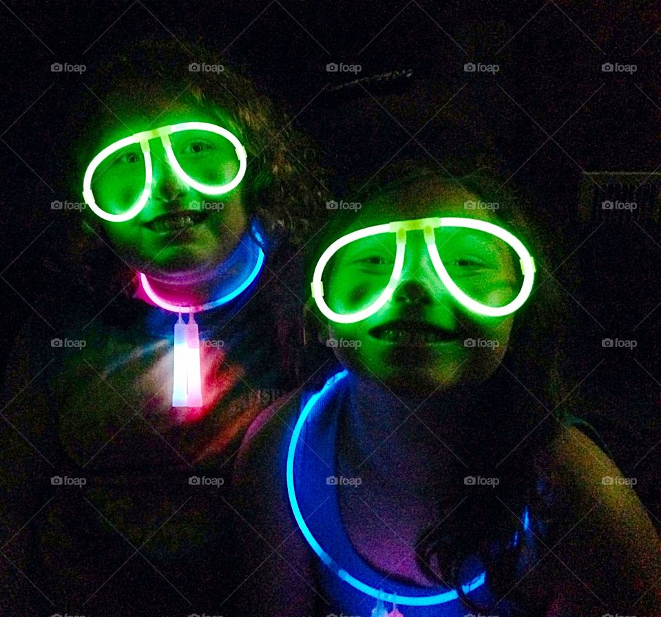 Neon Friends. Two young girls smiling in Glo-Stick glasses. 