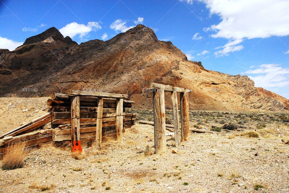 an acoustic sitting against an old wooden cattle ramp on Standbury Island in northern Utah against a rocky desert mountainside backdrop under a blue sky