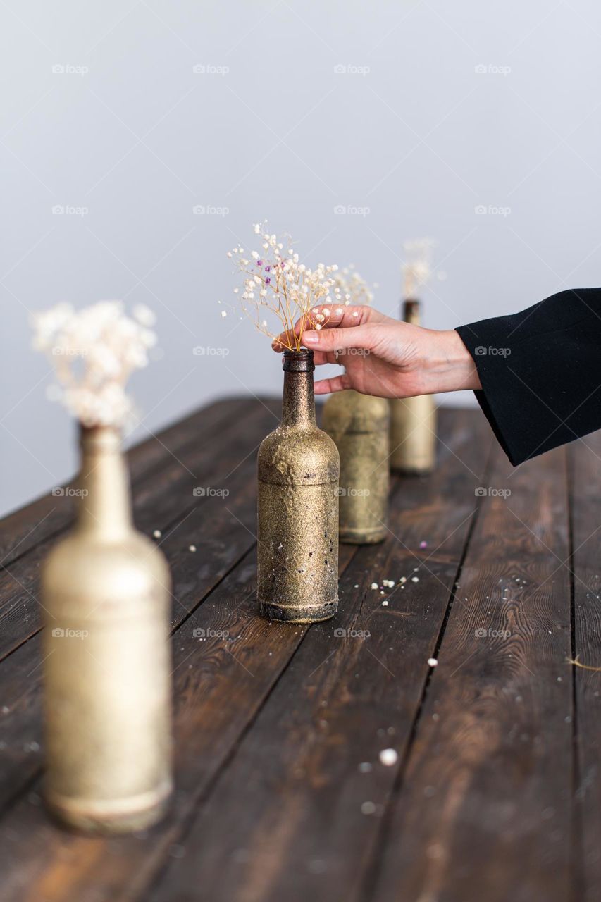 Hand putting dry flower in golden vase. Interior decoration. Woman hand. Minimalistic design