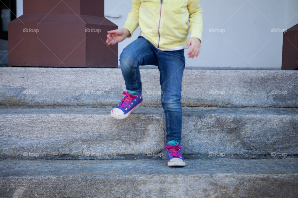 Bright purple and pink converse sneakers on a four year old little girl wearing jeans and a sweatshirt as she takes a step down. 
