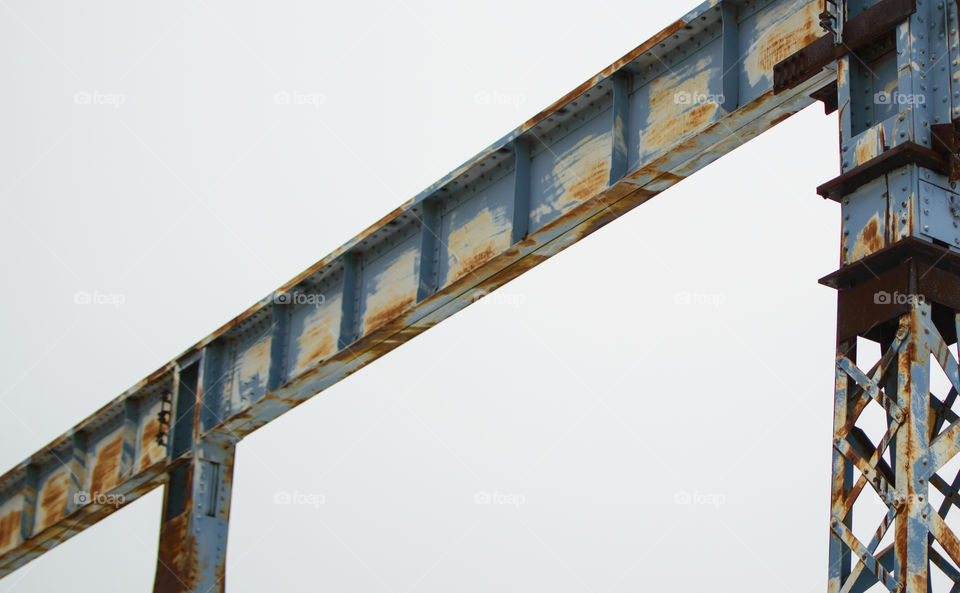 Old metal structure with peeling blue paint and rust against cloudy sky low angle view 