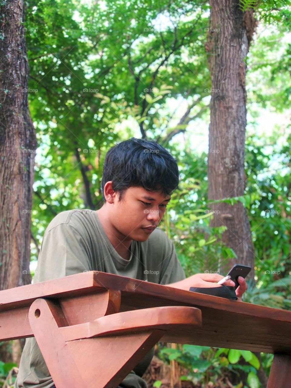 Young man is holding a cellphone in the forest in low angle view