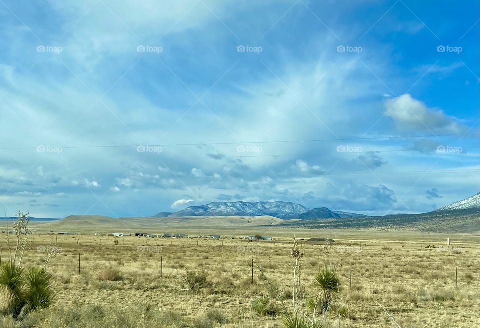 Cloudy blue skies in New Mexico desert with snow capped mountains in the background