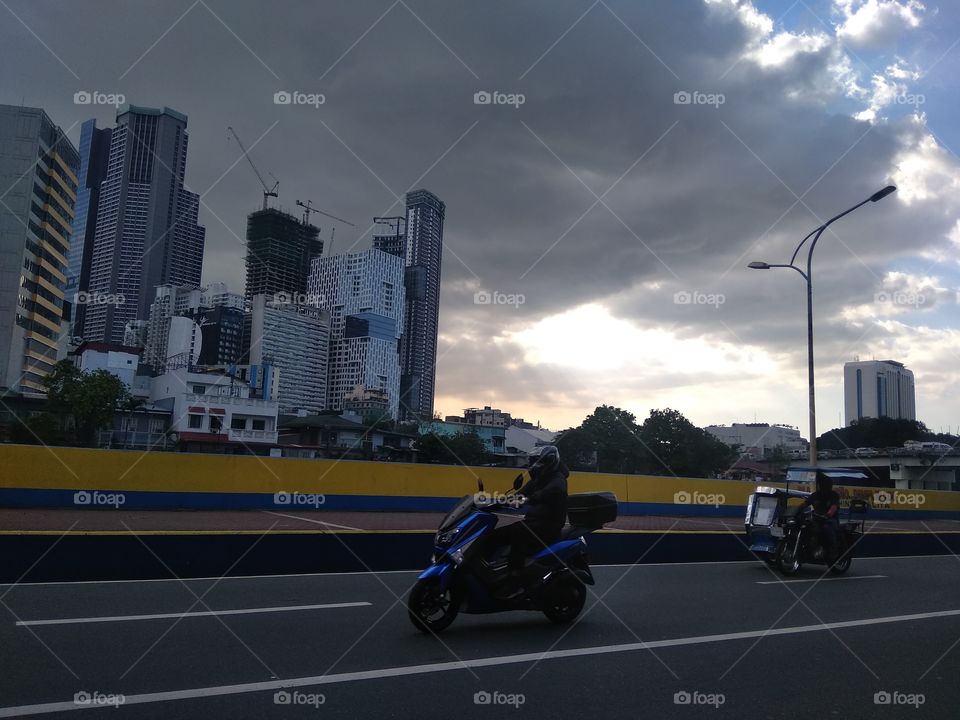 City View Night and day. It's a cloudy day. This big and wide cloud covering the background with beautiful peek of light. The buildings are shaded by this cloud. It's a beautiful view with motorcycles.