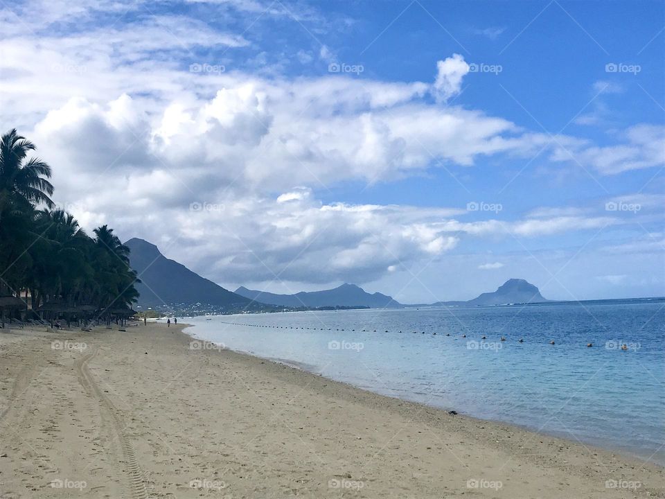 Coastal view with mountain and hills in distance. Golden sands, calm blue sea and a cloudy blue sky