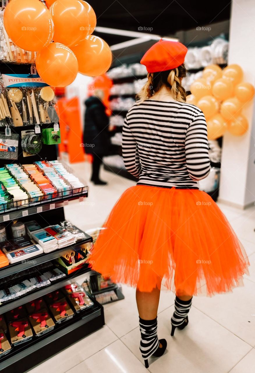 A girl in a bright orange skirt and orange beret walks through the store