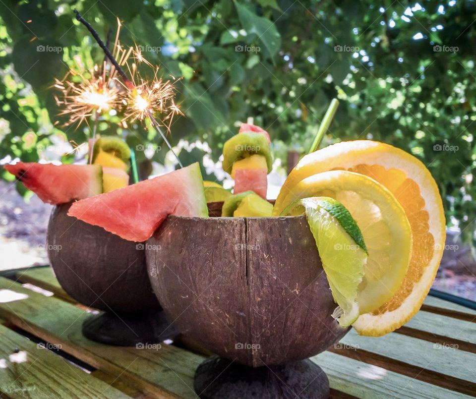 Fruity cocktails served in coconut shells and with sparklers, under a green and shady tree