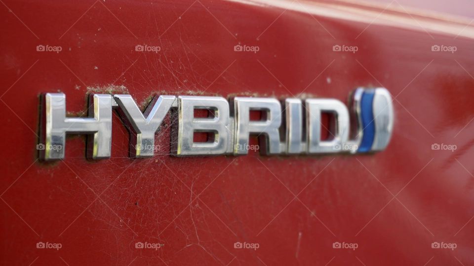 Hybrid symbol on a red car with some spider webs on it 