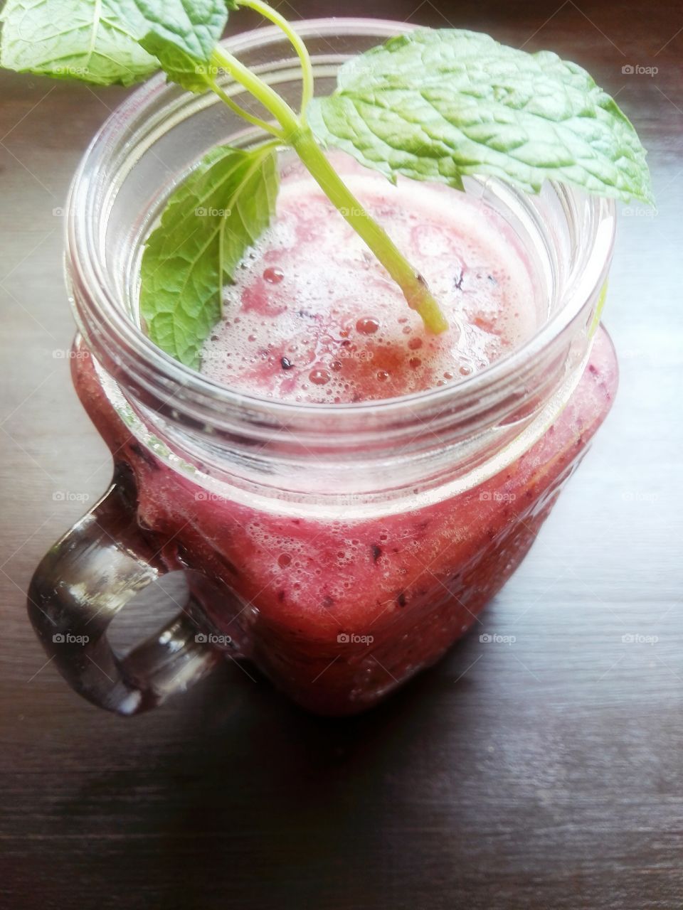 Red fruit smoothie with mint leaves on dark background