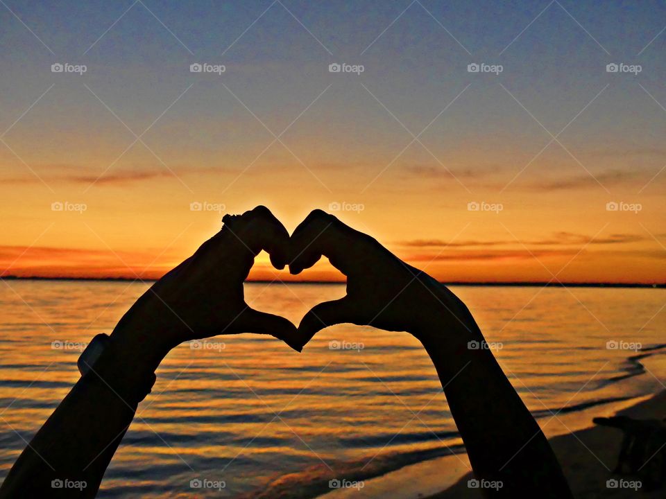 A heart-hand shape symbol captures a magnificent and colorful sunset. This sign  is used to express romance, affection and love