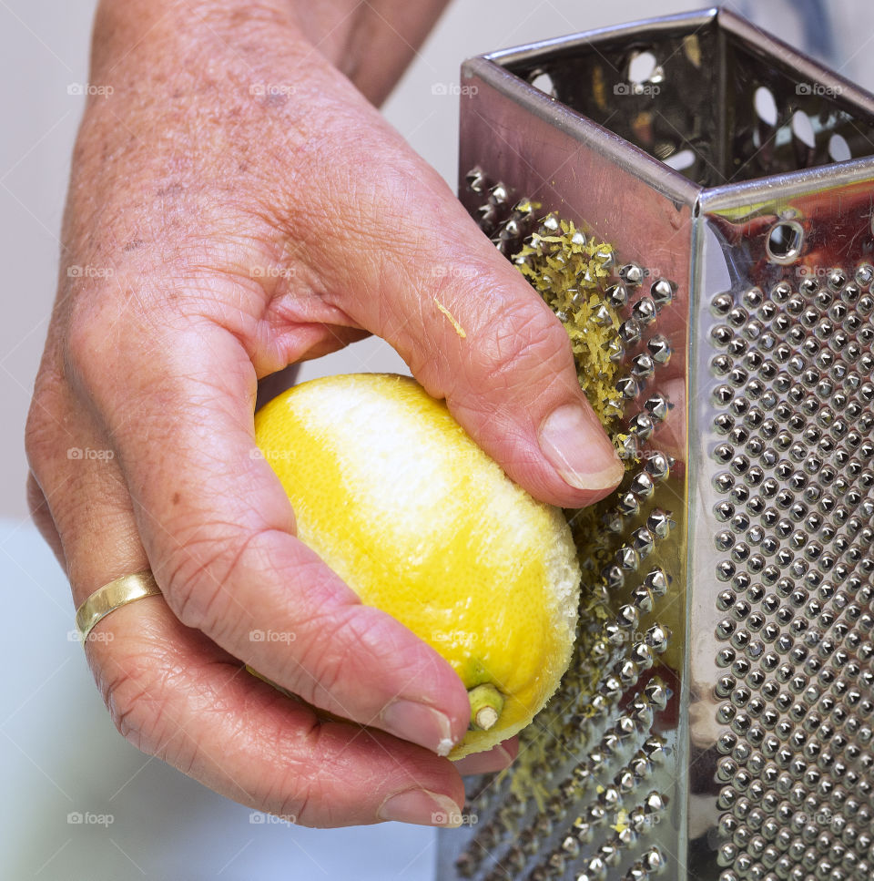 A woman's hand holds a lemon against  a metal grater to get rind.