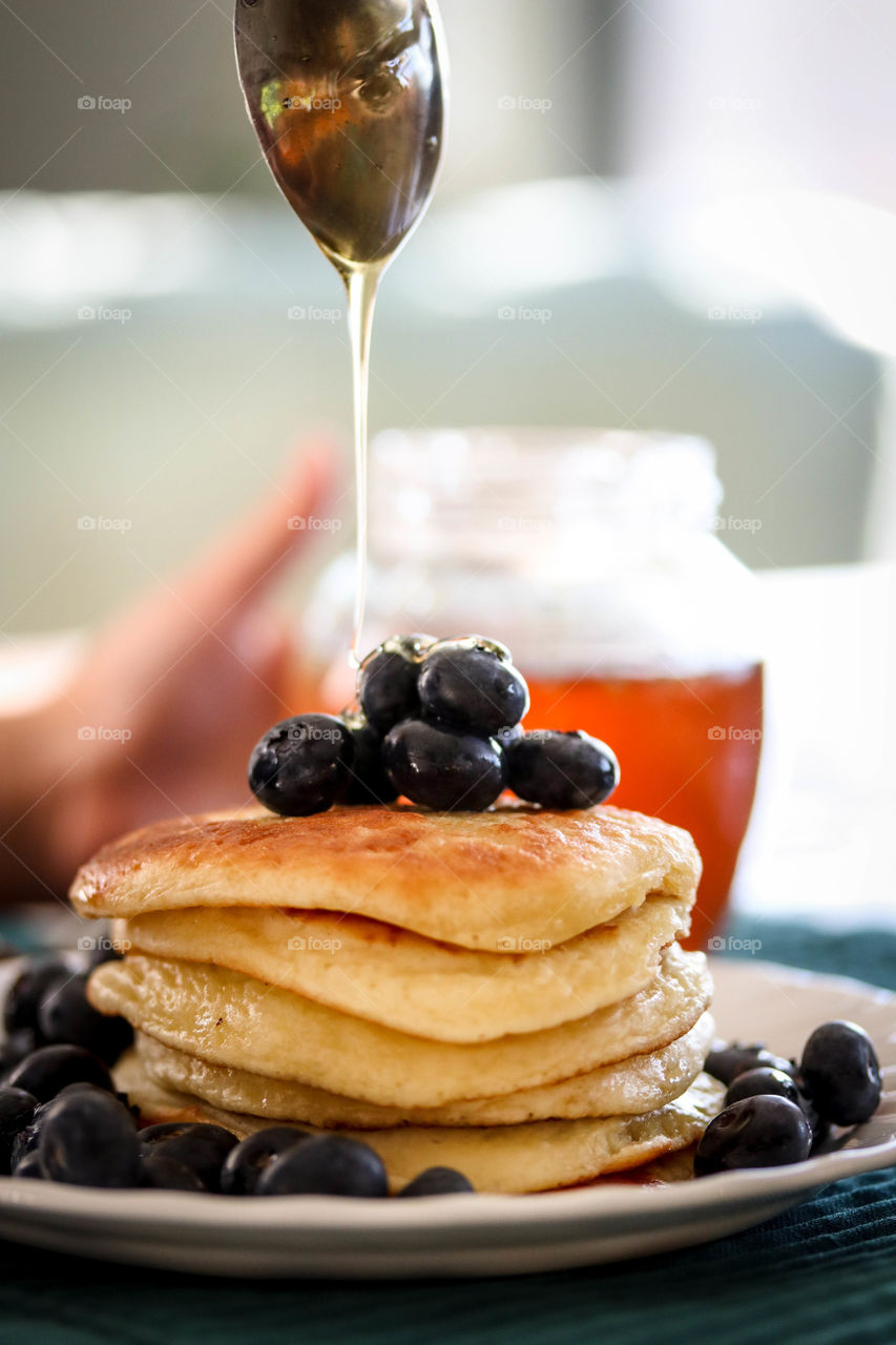 Pile of a freshly made golden pancakes with blueberries and honey