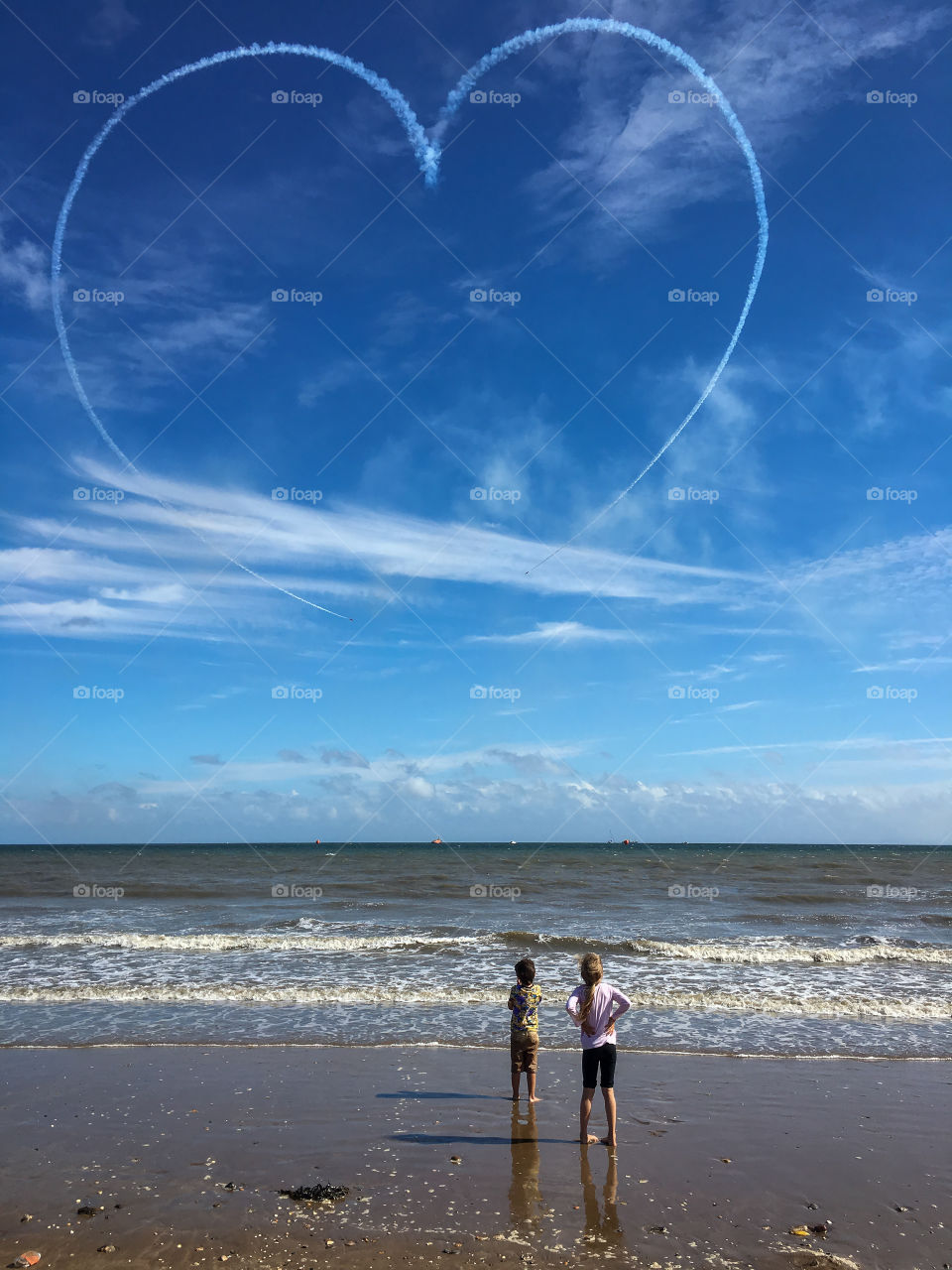 Two kids on the beach admire a heart in the sky