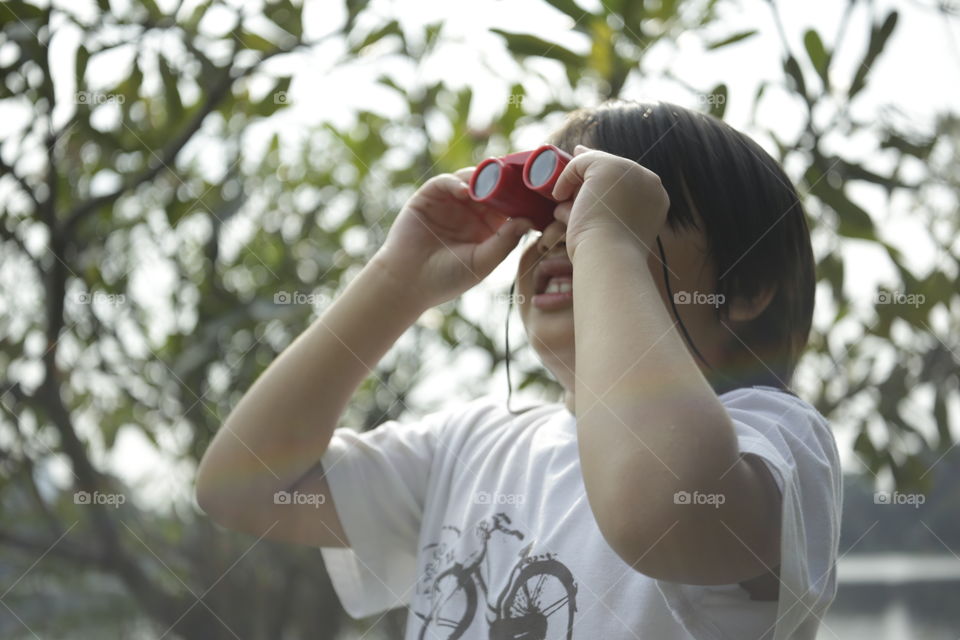 the adventurer, you boy looking through binoculars in the open outdoor with trees background out of focus