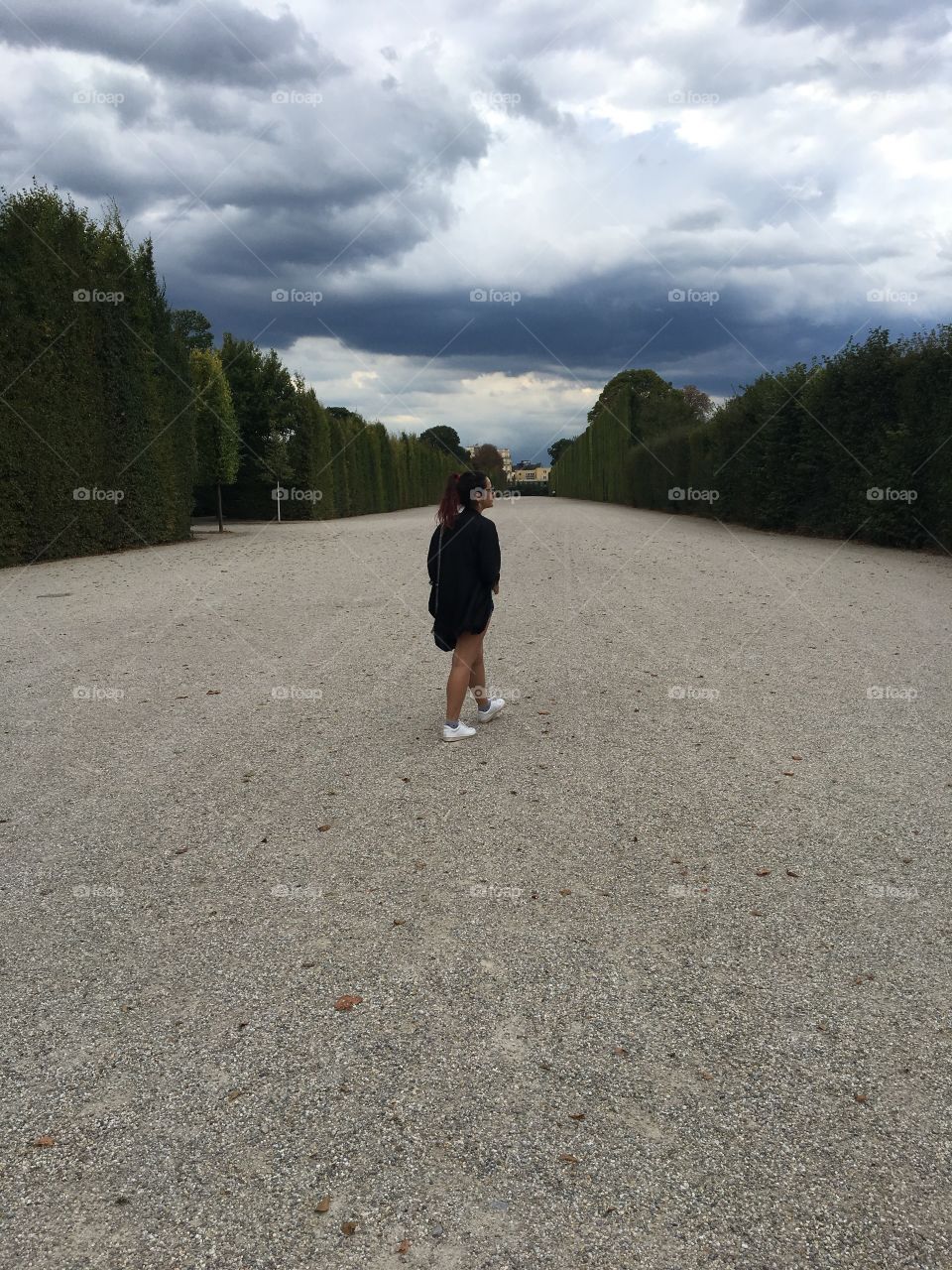A woman walking along a wide path with trees all around 