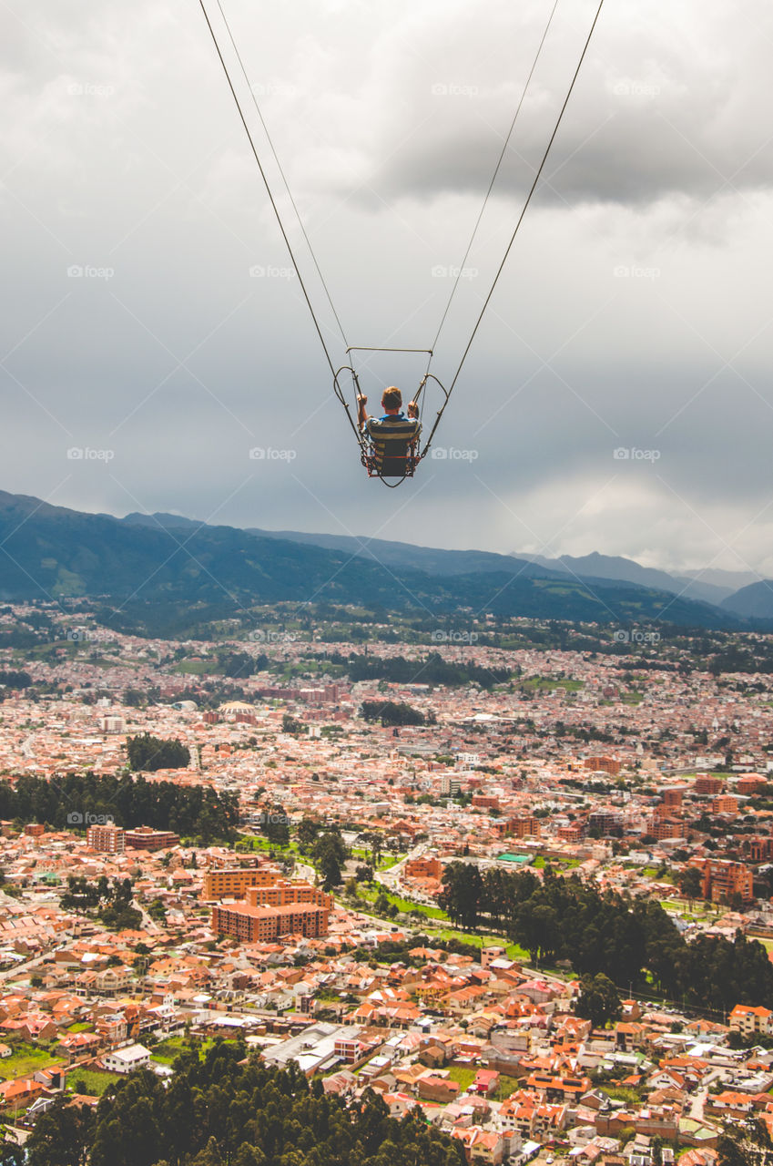 Man swinging on the edge of a cliff with the city in the background 