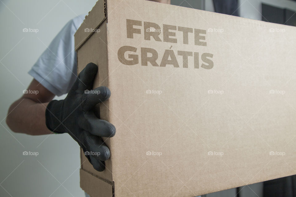 Detail of man with black gloves holding a cardboard box written free shipping to deliver products on gray background. Delivery concept. Delivery service concept. Copy space. Black friday concept.