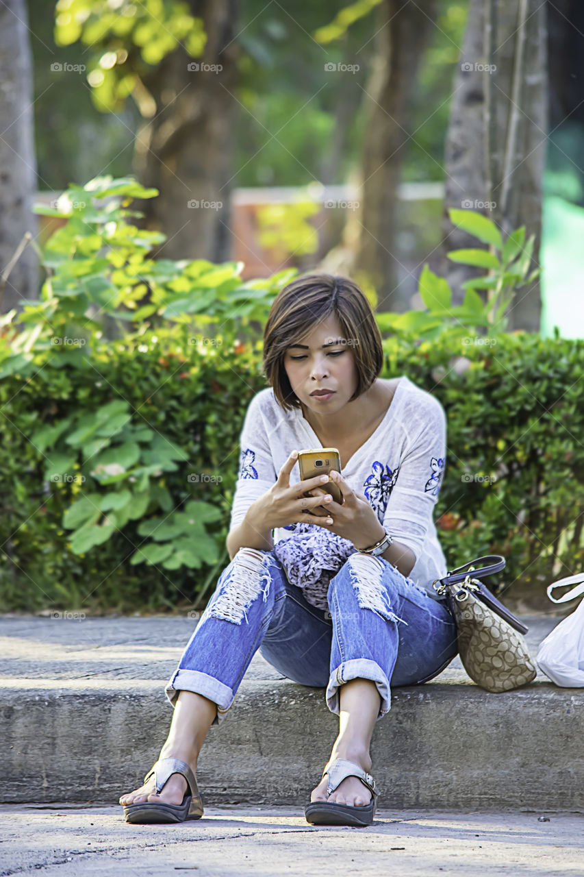 Asian women Sitting on the sidewalk along the street and play Mobile.