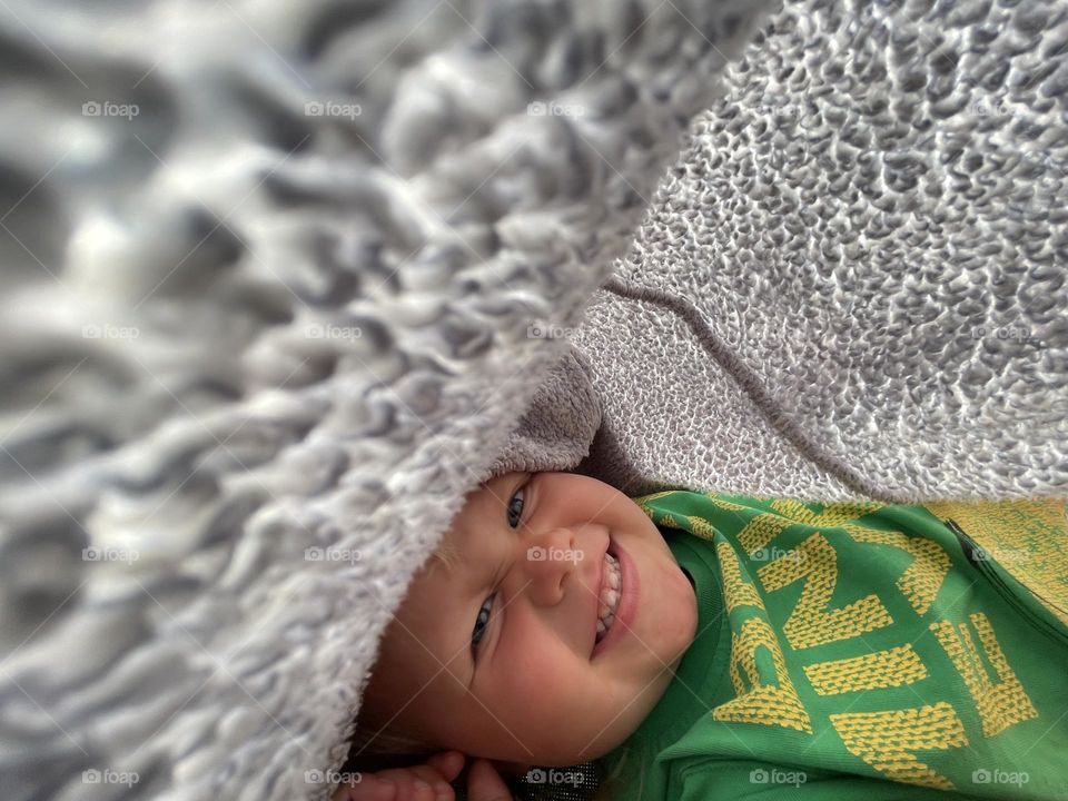 Little baby girl laying down in a trampoline and covering herself with a woollen blanket to protect her from a sun