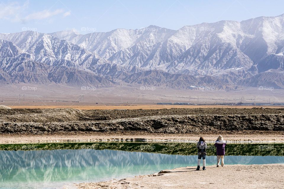 Two teenagers looking at a snow mountain in front of a crystal lake