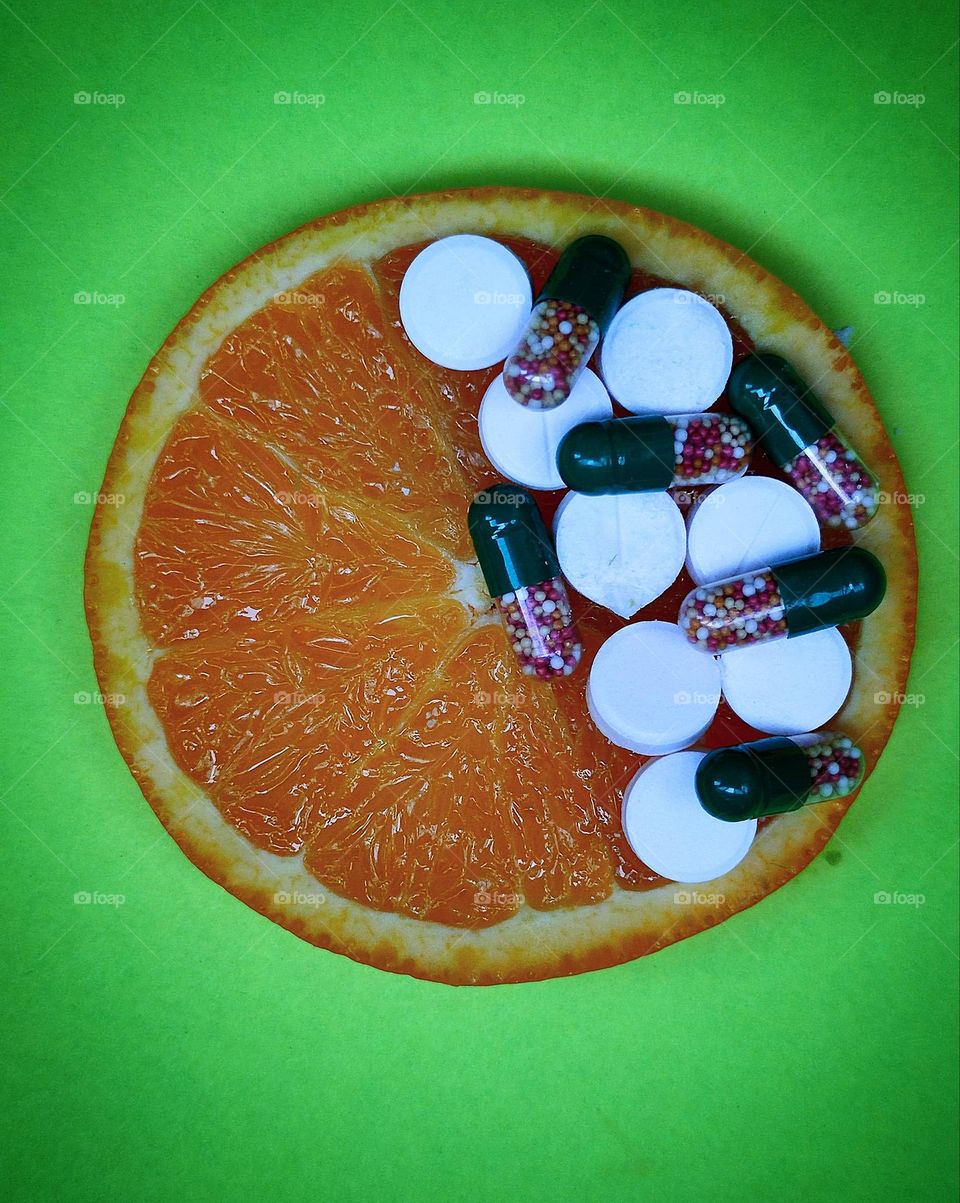 Healthy diet. Vitamins natural and in medicinal forms. On a green background lies a cut orange, half of which is filled with vitamins in capsules and white tablets. Selection for natural fruit