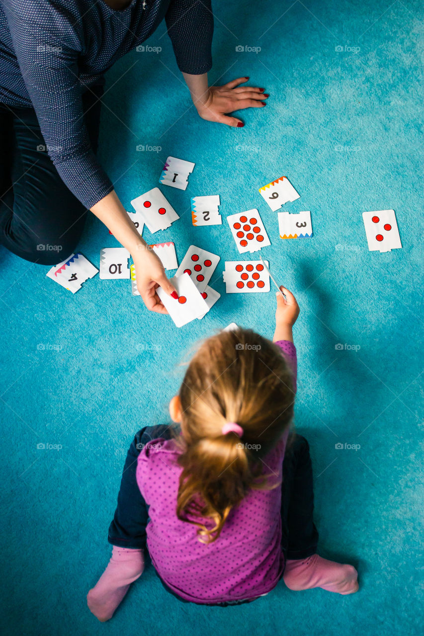 Mother teaching counting her little daughter using card game sitting on a carpet at home