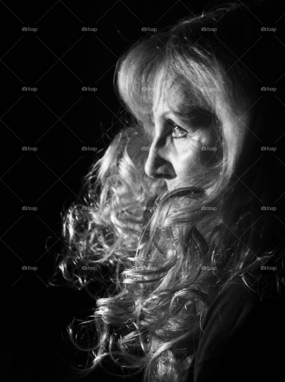 Artificial light on a blonde woman’s face and hair with a black background 