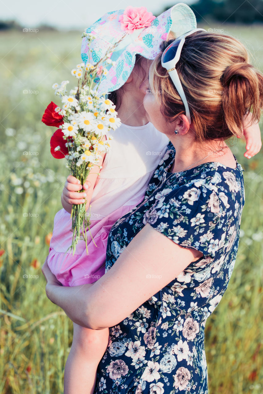 Mother and her little daughter in the field of wild flowers. Little girl picking the spring flowers for her mom for Mother's Day in the meadow. Girl handing the flowers to her mom. Nature scene, family time