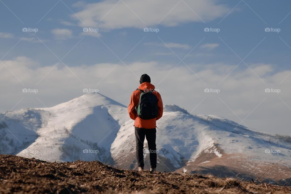 Rear view of male hiker standing on field against snowcapped mountains . 