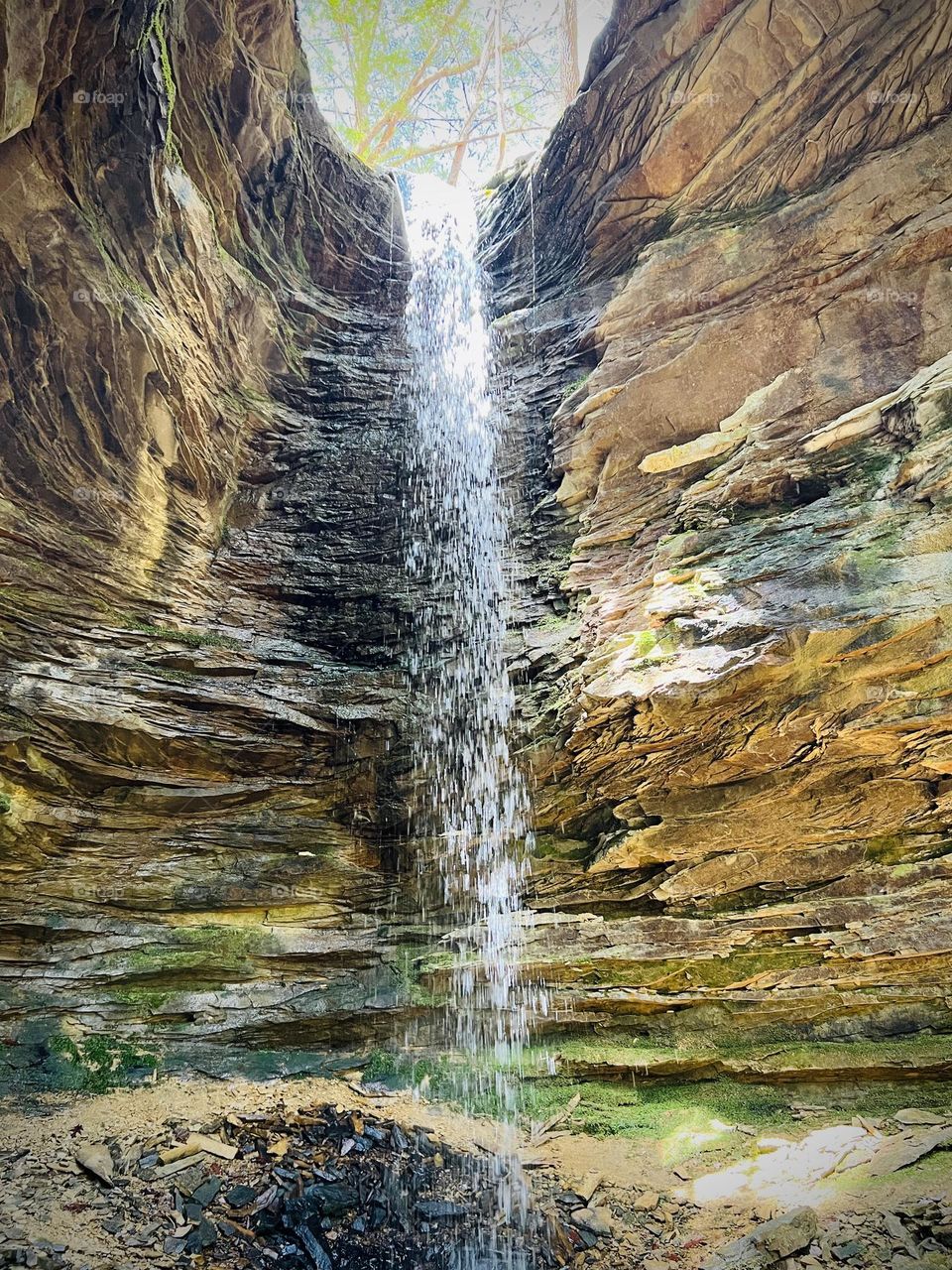 Looking up at a waterfall inside a small canyon. Millions of years of sedimentary rock surround the water.