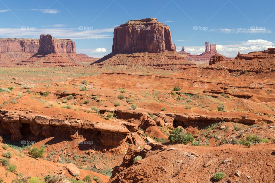 View towards Monument valley. Dry red landscape photo taken from Monument valley drive, Utah, USA. Several buttes in photo. Blue sky with few clouds