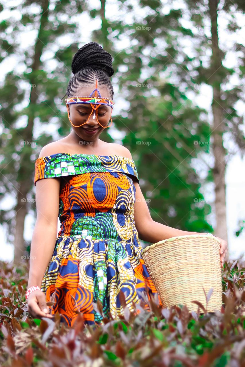 A beautiful Black African woman wearing traditional clothes in the purple tea farm with a beautiful smile on her face.