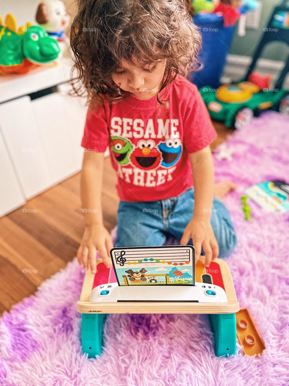 Toddler plays Einstein Piano, toddler playing piano with sheet music, toddler girl playing instrument, toddler girl wearing Sesame Street shirt, toddler girl plays Einstein Piano with sheet music, baby learning piano, toddler learning instruments